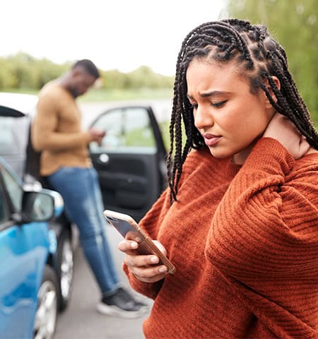 Woman holding her neck in pain while on the phone after a car accident, seeking care from an auto accident doctor in Encinitas